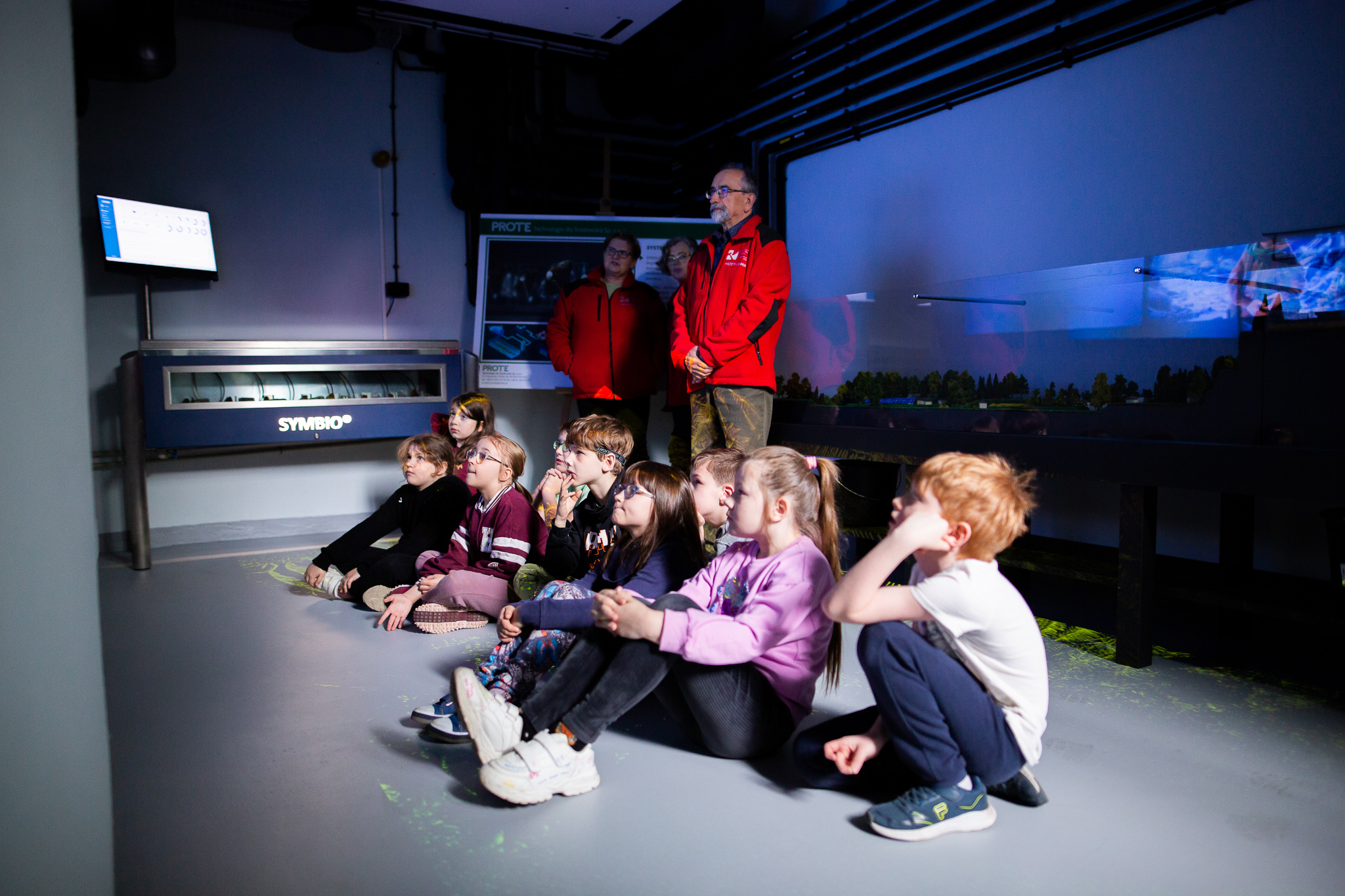 Dzieci szkół podstawowych podczas lekcji z edukatorem - oglądający film.