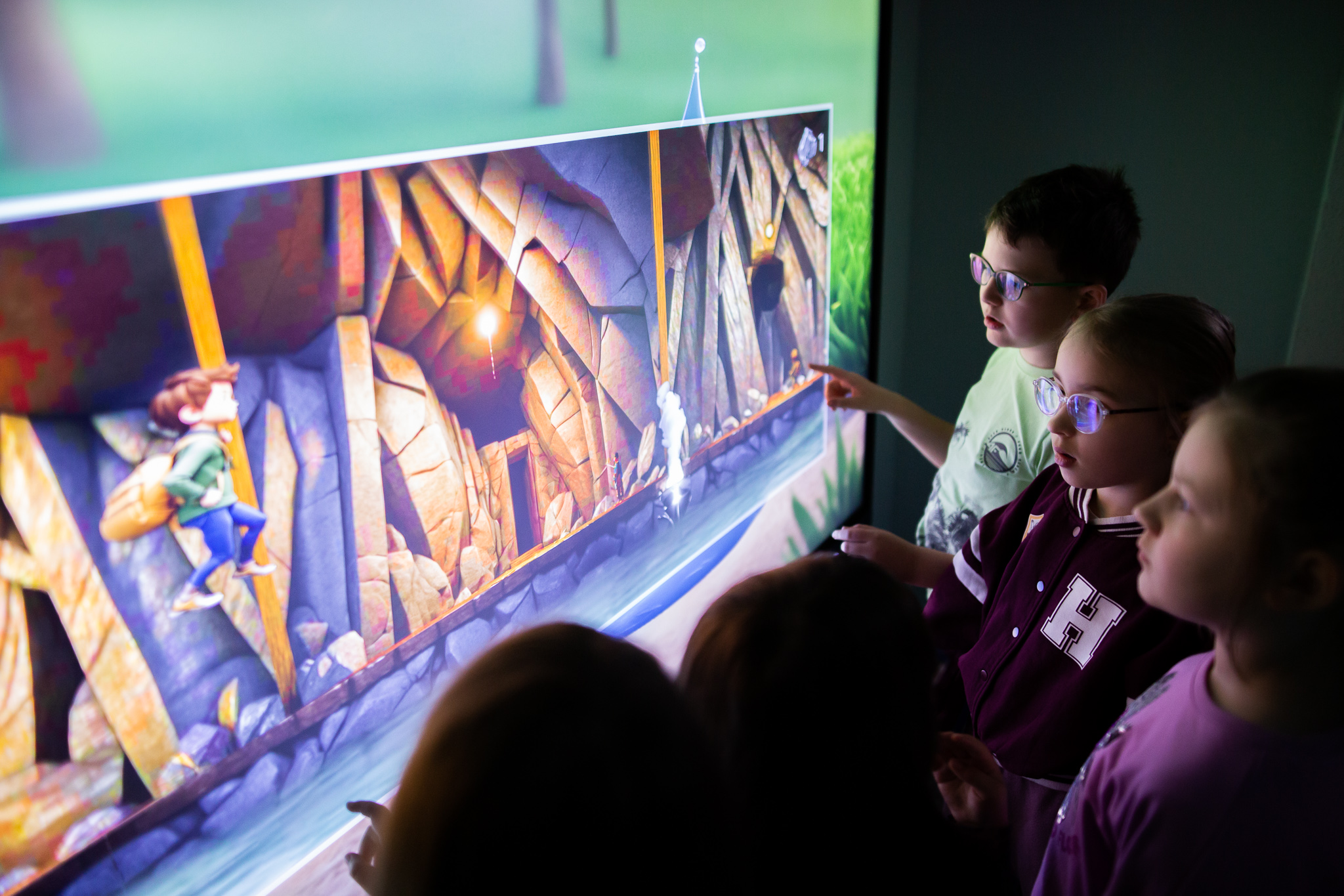 Dzieci podczas zajęć w Maszynowni Żywiołów grają w grę na dużym ekranie dotykowym.